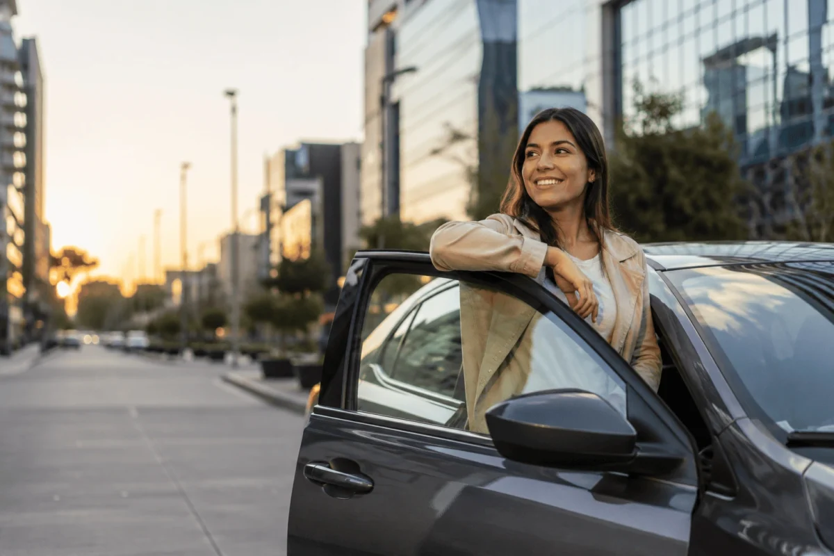 Mujer sonriente junto a su auto, protegida con seguro todo riesgo en Colombia